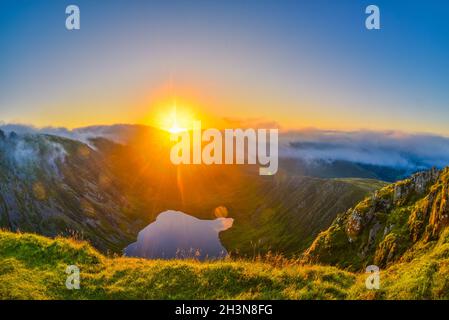 Erstaunlicher Sonnenaufgang auf dem Cadair Idris Berg in Snowdonia, Nordwales. Die Sonne scheint auf dem Gletschersee, die herrliche Wolkeninversion, die Berge umhüllt. Stockfoto