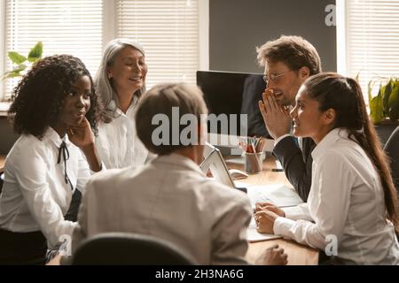 Lustige Geschäftstreffen im Büro. Büroangestellte beraten sich an ihrem Schreibtisch und lächeln. Hochwertige Fotos Stockfoto