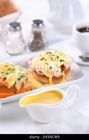 Hollandaise Buttersauce in einem Soße Boot zum Frühstück mit Eiern Benedict serviert - gebratenes englisches Brötchen, Stockfoto