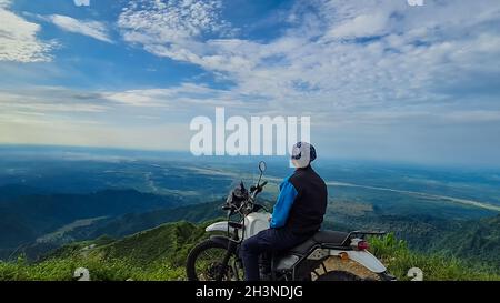 Der junge Mann, der auf dem Fahrrad auf der Bergspitze sitzt, mit einer faszinierenden Aussicht am Morgen, wurde auf dem kurseong darjeeling West bengal india aufgenommen. Stockfoto