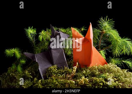 Origami Wolf und Fuchs auf grüner Moosinsel isoliert auf schwarzem Hintergrund Stockfoto