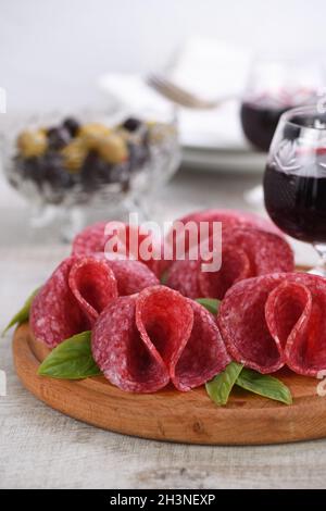 Leichte Mahlzeit Snack aus Salami in Form einer Blume mit einem Glas Sherry auf einer Holzschale gefaltet. Cl Stockfoto