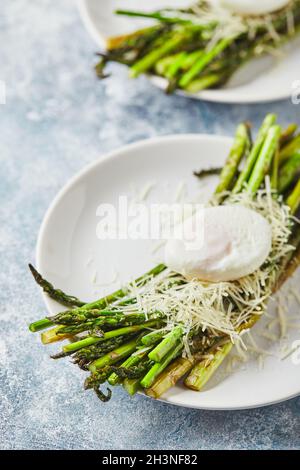 Grüner Spargel mit pochiertem Ei und Parmesan, vegetarisches Frühstück auf weißem Teller auf hellem Hintergrund. Stockfoto