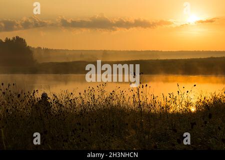 Ein Fischer bei Sonnenuntergang am Teich fängt Fische. Stockfoto