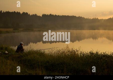 Ein Fischer bei Sonnenuntergang am Teich fängt Fische. Stockfoto