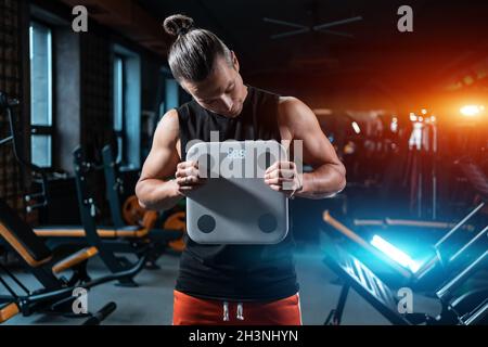 Junge attraktive Athlet männliche Gewicht mit Skala in der Turnhalle und Diät Stockfoto