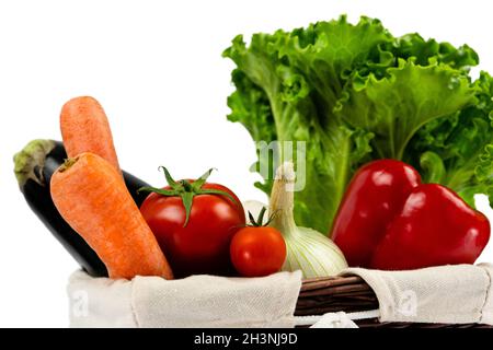 Frisches und reifes Gemüse in einem Weidenkorb. Gesundes veganes Essen. Gemüse aus dem Gemüsegarten auf weißem Hintergrund Stockfoto