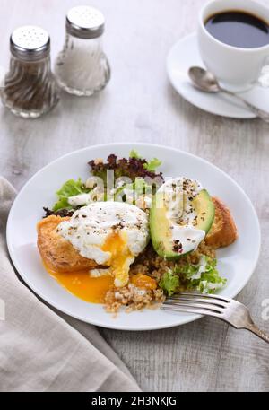 Ein gesunder und ausgewogener Frühstücksteller. Benedict's Ei breitet sich auf einem gerösteten Toast mit einem halben avoca aus Stockfoto