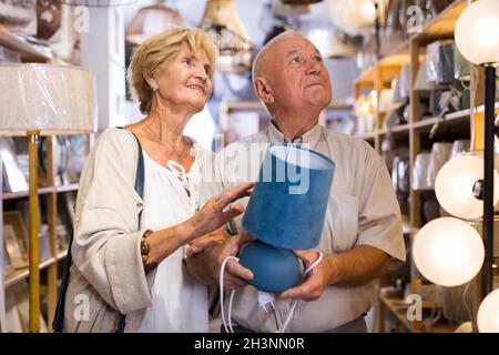 Ältere Männer und Frauen entscheiden sich für eine neue Tischleuchte für ihr Zuhause im Geschäft Stockfoto