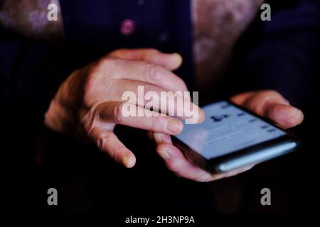 Authentische Lifestyle-Aufnahme einer älteren Frau, die per Smartphone mit Freunden über die Social-Media-App chatten kann. Hintergrund der Außerbetriebnahme von Technologie. Stockfoto