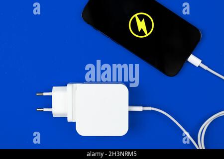 Blitzbares mobiles Ladegerät. Smartphone mit Energie-Symbol und Ladegerät auf blauem Hintergrund. Draufsicht, flach liegend Stockfoto