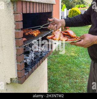 Grillen Sie mit verschiedenen Fleischsorten, die Sie mit einer Hand mit einer Pinzette grillen können, um die Wärmemenge zu kontrollieren Stockfoto