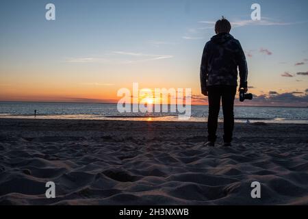 Silhouette eines jungen Fotografen, der am Strand fotografiert, Sonnenuntergangsszene Stockfoto