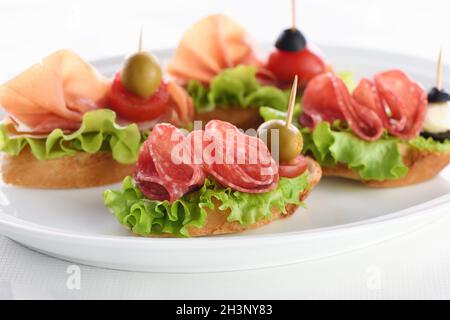 Zarte Baguette-Häppchen mit Blattsalat, Salami oder Parmaschinken, Tomaten, Mozzarella und Oliven. Feinkostgeschäft Stockfoto