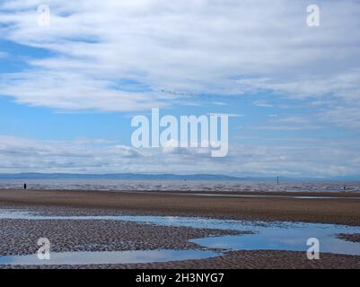 Der Strand von blundell Sands in southport mit Wellen, die am Strand brechen und der küste von mersey in der Ferne und einem Schwarm o Stockfoto