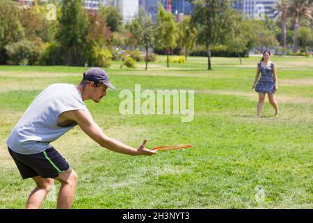 Junger Mann und Freundin, die am sonnigen Tag im Park mit fliegender Scheibe spielen. Paar sportliche Aktivitäten, Freizeitkonzepte Stockfoto