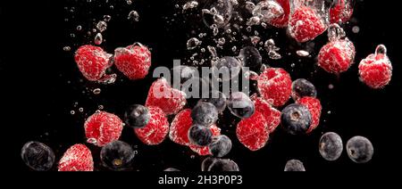 Heidelbeeren und Himbeeren, die mit Luftblasen und ins Wasser spritzen Sinkend auf schwarz Stockfoto