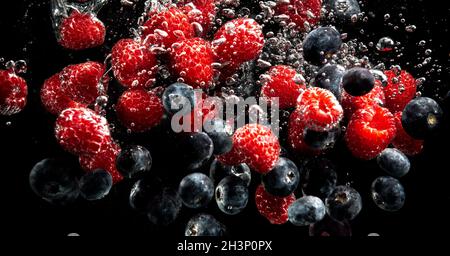 Heidelbeeren und Himbeeren, die mit Luftblasen und ins Wasser spritzen Sinkend auf schwarz Stockfoto