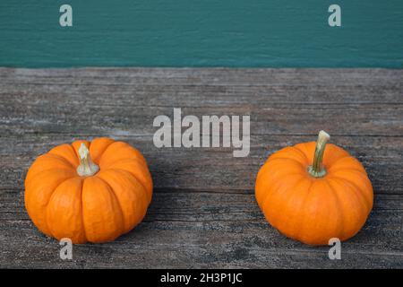 Zwei kleine orangefarbene Kürbisse auf einem Holzdeck mit blaugrünem Klappbretthintergrund mit Kopierfläche Stockfoto