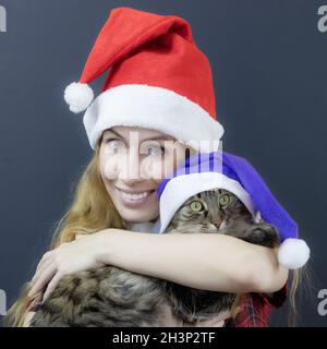Lächelnde Dame santa umarmt tabby Katze trägt lila weihnachtsmann Hut Stockfoto