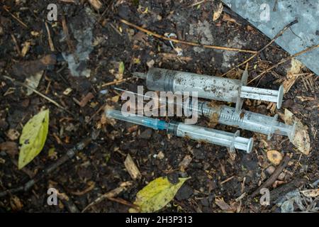 Ein Haufen von gebrauchten schmutzigen Spritzen, die nach der Medikamenteninjektion auf dem Boden im Freien lagen, war ausgezogen Stockfoto