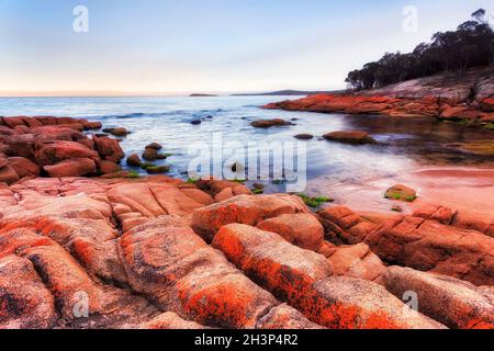 Kleiner roter Sandstrand an der Coles Bay an der Ostküste Tasmaniens bei Sonnenaufgang - malerische rote Granitfelsen, die von Flechten bemalt sind. Stockfoto