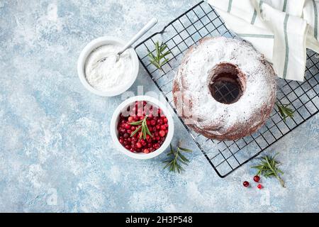 Schokoladenkuchen mit Puderzucker bestreut auf einem Metalldrahtgestell, Puderzucker und Preiselbeeren in Schalen, für Dekorationen vorbereitet Stockfoto