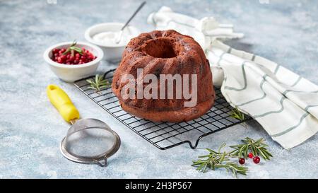 Schokoladenkuchen auf einem Metalldrahtgestell, Puderzucker und Preiselbeeren in Schüsseln Stockfoto