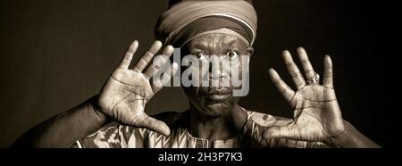 Afrikanischer Mann in traditioneller Kleidung, lächelnd, auf grauem Hintergrund Stockfoto