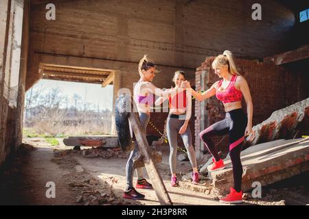 Nach dem Training klatschen Mädchen die Hände und lächeln positive Energie. Gruppenfitness-Leute feiern Erfolg in verlassenen Fabrik, heißen Sommertag Sonnenschein. Stockfoto