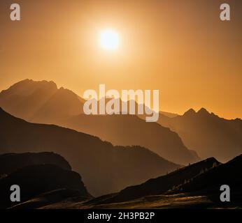 Die Sonne scheint am Abend, der Himmel ist trüb und die Aussicht auf die Silhouetten der Berge Stockfoto