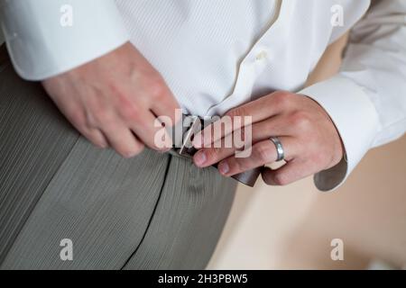 Ein Mann in Hose und Hemd knöpfte einen schwarzen Ledergürtel. Bräutigam Dress up ein Gürtel mit Schnalle. Geschäftsmann tragen Lederstil Stockfoto