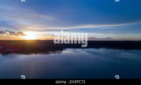 Luftaufnahme eines schönen und dramatischen Sonnenuntergangs über einem Waldsee, der sich im Wasser spiegelt, Landschafts-Drohne aufgenommen Stockfoto