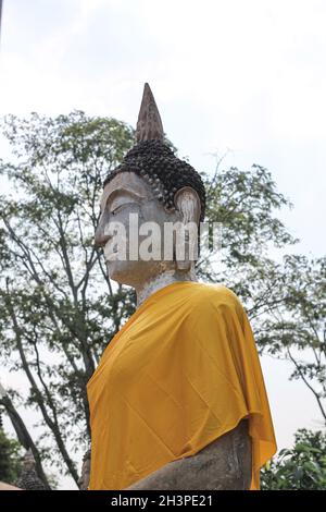 Blick aus dem niedrigen Winkel auf eine Buddha-Statue mit gelbem Tuch in der historischen Stätte Ayutthaya, Thailand Stockfoto