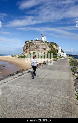 Eine Frau, die am Wellenbrecher von Nobbys Head - Newcastle Harbour entlang geht. Newcastle ist Australiens zweitälteste Stadt und Gebiete wie Nobbys Lighthous Stockfoto