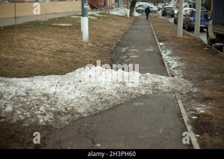 Schnee auf der Straße. Auf dem Asphalt liegt ein Haufen Schnee. Schneewehe im Park. Stockfoto