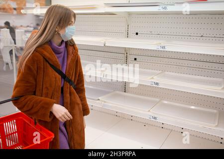 Junge Frau in medizinischer Gesichtsmaske und leeren Regalen im Supermarkt. Stockfoto