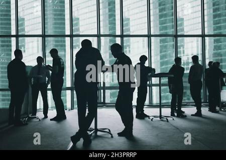 Mehrere Silhouetten von Geschäftsleuten interagieren Business Center und große Fenster Hintergrund. Gesichter geändert. Stockfoto