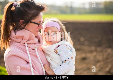 Mutter und Kind, die auf einer Landstraße zwischen landwirtschaftlichen Feldern in Richtung von Wald in Richtung von Verderbnissen gehen. Stockfoto