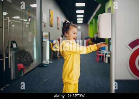 Kind Mädchen mit automatischen Alkohol-Gel-Spender Sprühen auf Hände Desinfektionsmaschine antiseptische Desinfektionsmittel, neues normales Leben af Stockfoto