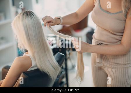 Friseur Frau macht Haarerweiterungen für junge Frau mit blonden Haaren im Schönheitssalon. Professionelle Haarverlängerung. Stockfoto