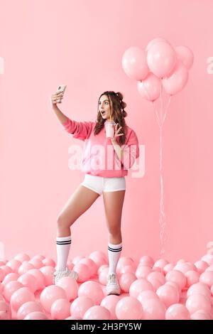 In voller Länge Porträt von trendigen jungen Frau macht Selfie-Foto auf dem Smartphone halten Milk Shake Stockfoto