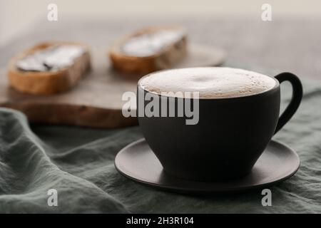 Cappuccino in schwarzer Tasse mit Ciabatta-Scheiben mit Schokoladenaufstrich auf dem Hintergrund, flacher Fokus Stockfoto