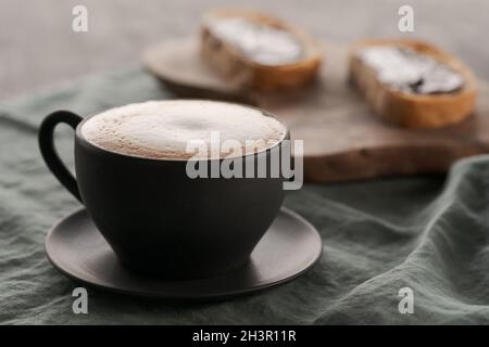 Cappuccino in schwarzer Tasse mit Ciabatta-Scheiben mit Schokoladenaufstrich auf dem Hintergrund, flacher Fokus Stockfoto