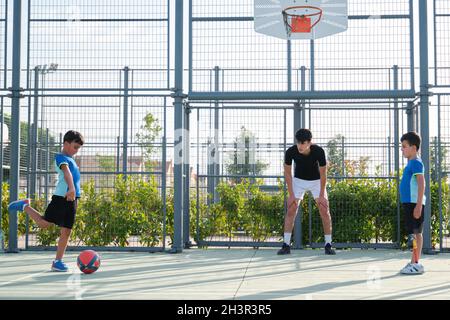 Couch, die mit zwei Schülern Fußball spielt. Stockfoto