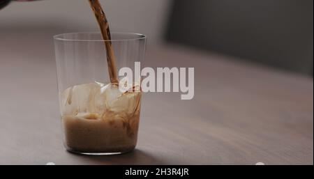 Gießen Sie Cola in Glas mit Eis auf Walnusstisch mit Kopierraum, breites Foto Stockfoto