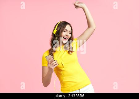 Glückliche junge Frau, die mit Kopfhörern Musik hört und tanzt, genießt Lieblingslieder Stockfoto