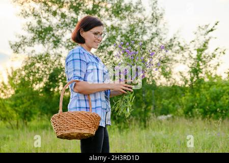 Lächelnde Frau mittleren Alters mit einem Korb und einem Blumenstrauß in der Natur Stockfoto