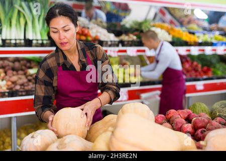 Verkäuferin legt Obst und Gemüse in den Regalen im Lebensmittelgeschäft aus Stockfoto