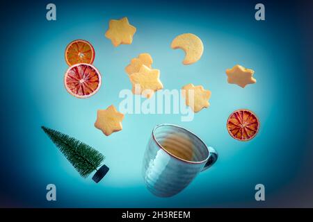 Fliegende Butterkekse, Tee und ein Weihnachtsbaum auf dunkelblauem Hintergrund Stockfoto